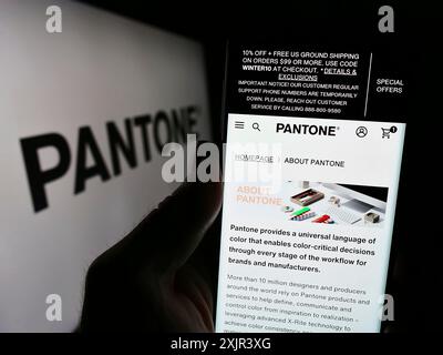 Stuttgart, 28.12.2023: Person, die ein Mobiltelefon hält, mit Website des US-amerikanischen Farblösungsunternehmens Pantone LLC vor dem Geschäftslogo. Fokus Stockfoto