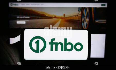 Stuttgart, 28.12.2023: Person, die ein Mobiltelefon mit dem Logo der US-amerikanischen Finanzgesellschaft First National Bank Omaha (FNBO) vor dem Geschäft hält Stockfoto