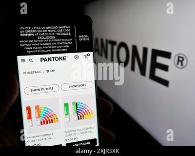 Stuttgart, Deutschland, 28.12.2023: Person, die ein Mobiltelefon hält, mit Webseite des US-amerikanischen Farblösungsunternehmens Pantone LLC vor dem Firmenlogo. Konzentrieren Sie sich auf Stockfoto