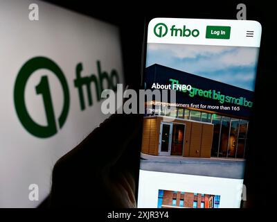 Stuttgart, 28.12.2023: Person, die ein Mobiltelefon hält, mit Website des US-amerikanischen Finanzunternehmens First National Bank Omaha (FNBO) vor dem Logo. Stockfoto