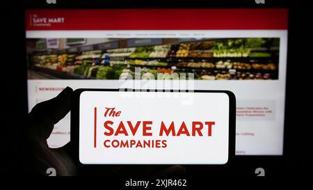 Stuttgart, Deutschland, 02.03.2024: Person mit Handy mit Logo des US-Supermarktunternehmens The Save Mart Companies vor der Business-Webseite. Stockfoto