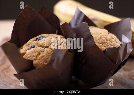 Frisch gebackene Bananenschokolade-Chips-Muffins in braunem Pergamentpapier, auf einem Holzschneidebrett neben einem Haufen reifer Bananen. Stockfoto