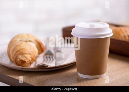 Eine Nahaufnahme eines klassischen Buttercroissants auf einem rustikalen weißen Teller, begleitet von einer Gabel und einem Messer auf einer Serviette. Das goldbraune Croissant Stockfoto