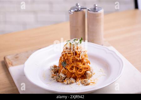 Ein wunderschön überzogener Turm aus Spaghetti, ummantelt mit einer reichhaltigen Tomatensauce, garniert mit frischen Basilikumblättern und garniert mit geriebenem Käse. Stockfoto