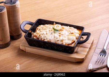 Eine köstliche, käsige Lasagne, serviert in einem schwarzen Keramikgericht, garniert mit geschmolzenem Mozzarella und garniert mit einem Basilikumblatt. Stockfoto