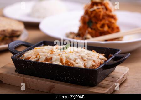 Eine köstliche, käsige Lasagne, serviert in einem schwarzen Keramikgericht, garniert mit geschmolzenem Mozzarella und garniert mit einem Basilikumblatt. Stockfoto