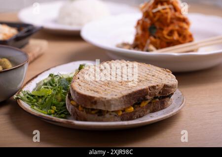 Ein gesundes Sandwich mit Spinat, Mais und Käse, serviert auf Vollkornbrot mit einer Beilage aus frischem grünem Salat. Stockfoto