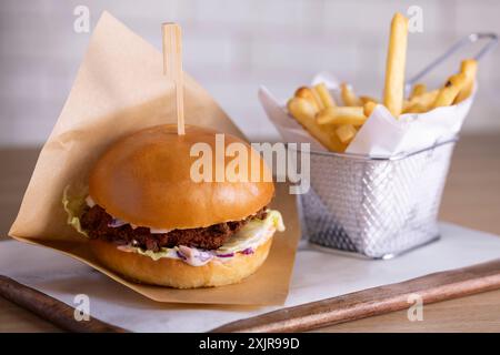 Köstlicher knuspriger Hähnchenburger mit frischem Krautsalat und einem weichen Brioche-Brötchen, serviert neben goldenen Pommes frites auf einem Holztablett. Stockfoto