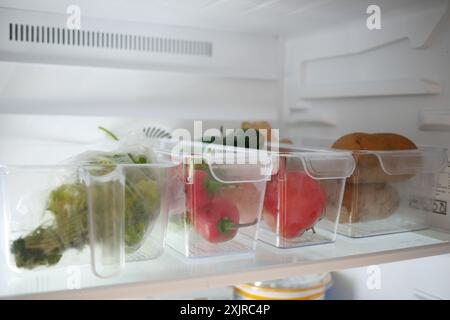 Plastikbehälter mit verschiedenen Früchten in einem offenen Kühlschrank. Stockfoto