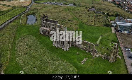 Blick aus der Vogelperspektive auf die antiken Ruinen eines großen Steingebäudes, umgeben von grünen Feldern und einem kleinen Teich. In der Nähe befinden sich moderne Gebäude und eine Straße. Stockfoto