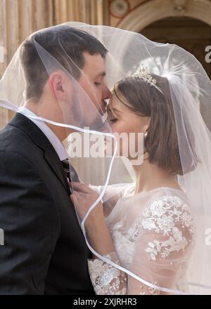 Hochzeitsporträt der Braut und des Bräutigams. Glückliche Braut und Bräutigam umarmen sich unter einem Schleier, sanfte Berührung. Liebe, neue Familie, Zärtlichkeit Stockfoto