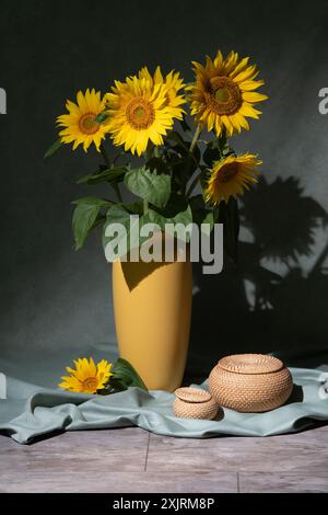 Ein Strauß großer Sonnenblumen in einer gelben Vase, neben zwei runden Kästen. Stillleben Stockfoto