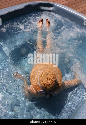 Junge Frau mit Strohhut und sehr langen Beinen, die sich während einer Hydromassage-Behandlung in einem exklusiven Luxusresort in der Badewanne entspannen Stockfoto