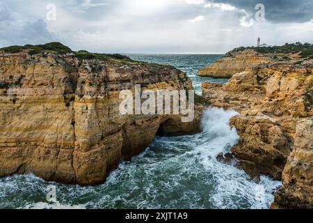 Die felsige Küste von Carvoeiro mit dem entfernten Leuchtturm von Alfanzina, Portugal Stockfoto