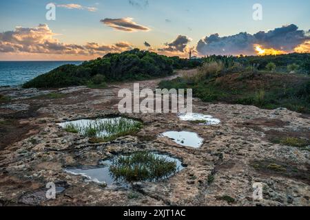 Die felsige Küste von Carvoeiro mit dem entfernten Leuchtturm von Alfanzina, Portugal Stockfoto