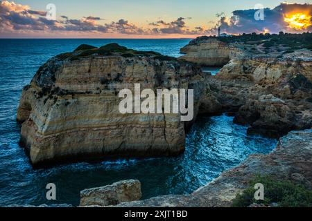 Die felsige Küste von Carvoeiro mit dem entfernten Leuchtturm von Alfanzina, Portugal Stockfoto