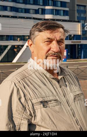 Ein attraktiver, jugendlicher, grauhaariger Mann von 70 Jahren vor dem Hintergrund von Bürogebäuden aus Spiegelglas. Porträt einer älteren grauhaarigen M Stockfoto