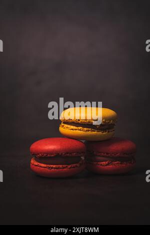 Eine Nahaufnahme von drei Makaronen, die übereinander gestapelt sind. Die Macarons sind in einem Muster aus Rot, Gelb und Rot angeordnet. Sie werden gegen einen gesetzt Stockfoto