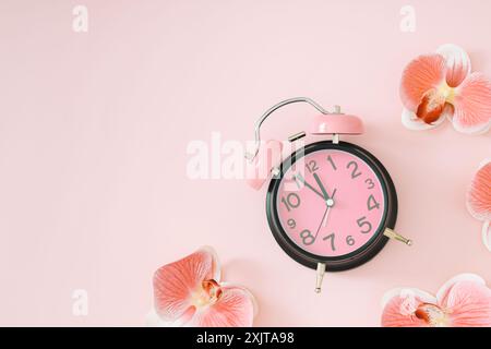 Pastellrosa und schwarzer Wecker und weiße und rosa Orchideenblüten auf hellem pastellrosa Hintergrund mit Kopierraum. Minimales Zeitkonzept. Stockfoto