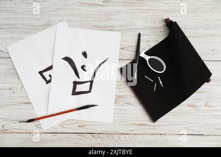 Kalligraphie. Papiere mit geschriebenem Wort Finish in Chinesisch, Tintenfass, Füllfederhalter und Pinsel auf weißem Holztisch, flach gelegt Stockfoto