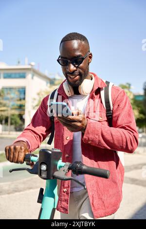 Junger afrikanischer Schwarzer Tourist, der ein Smartphone mit einem Elektrofahrrad in der Stadt hält. Stockfoto