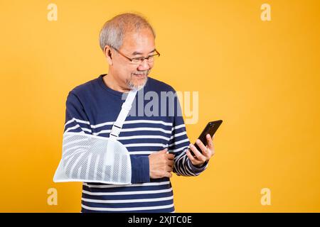 Porträt asiatischer alter Mann warf seinen Arm und hielt das Handy-Studio isoliert gelben Hintergrund Stockfoto