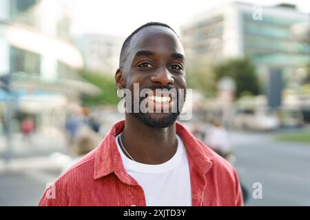 Glücklicher junger afrikanischer Mann, der auf der Stadtstraße steht und in die Kamera schaut. Hochformat Stockfoto