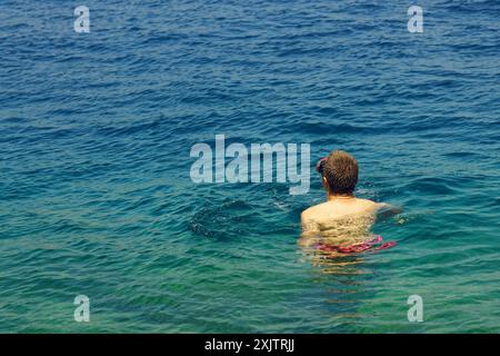 Ein Mann, der von hinten fotografiert wurde, schwimmt im klaren, hellen Wasser der Adria. Badeurlaub in Kotor Bay, Montenegro Stockfoto