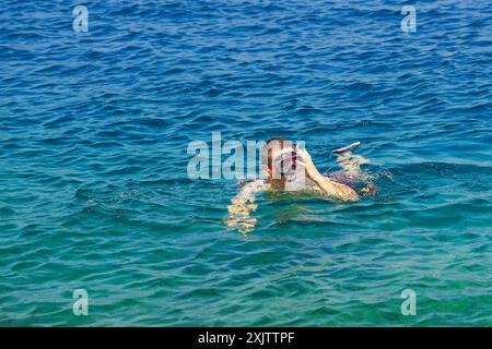 Ein junger Mann, der in hellblauem Wasser schwimmt, passt die Maske auf seinem Gesicht an. Ein Tourist, der in der Nähe der Halbinsel Lustica schnorchelt - Sommeraktivitäten Stockfoto