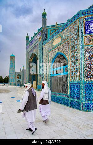 Zwei afghanische Männer in traditioneller Kleidung gehen am Schrein von Hazrat Ali, bekannt als Blaue Moschee, in Mazar-i-Sharif, Nordafghanistan vorbei. Stockfoto