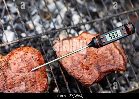 Gegrilltes Steak auf dem Grill mit digitalem Fleischthermometer, das 59 °C Innentemperatur anzeigt und eine mittlere Garbarkeit anzeigt Stockfoto
