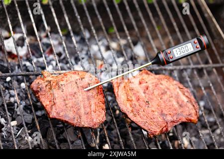 Gegrilltes Steak auf dem Grill mit digitalem Fleischthermometer, das eine Innentemperatur von 130 °F anzeigt, die mittelschwere, seltene Garung anzeigt Stockfoto