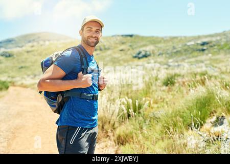 Mann, Rucksack und Wanderportrait in der Natur für Fitness-Abenteuer, Cardio und Spaziergänge, um die Umgebung zu erkunden. Wanderer, Person und Trekking auf Schotter Stockfoto