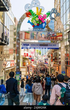 Der berühmte Eingangsbogen am Anfang der Takeshita Straße in Harajuku während des Tages, mit der Straße dahinter, voll mit Einkäufern in der Sonne. Stockfoto