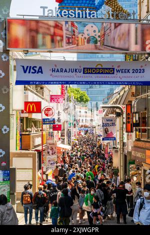 Der berühmte Eingangsbogen am Anfang der Takeshita Straße in Harajuku während des Tages, mit der Straße dahinter, voll mit Einkäufern in der Sonne. Stockfoto