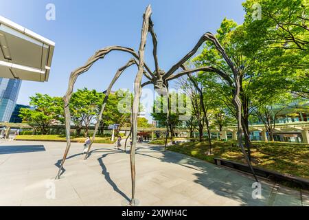 Die Maman Spider Skulptur am Mori Tower in den Roppongi Hills in Tokio. Das Kunstwerk steht mit einer Kolonnade aus Bäumen und einem überdachten Gang dahinter. Stockfoto