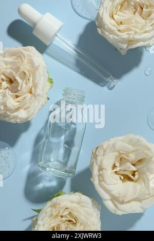 Schöne Rosenblüten, Kosmetikflasche, Pipette und Tropfen Serum auf hellblauem Hintergrund, flache Lay Stockfoto