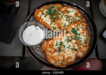 Ein Teller mit gebratenen Kartoffelpfannkuchen mit Petersilie und einer Seite Sauerrahm. Stockfoto