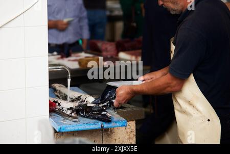 Ein Fischhändler putzt frischen Fisch an einem Marktstand mit einem Messer und fließendem Wasser in Funchal, Madeira, Portugal Stockfoto