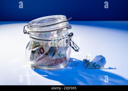 Gefaltete Banknoten als Ersparnis in einem offenen Glas mit einem harten blauen Schatten Stockfoto