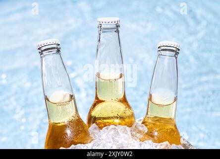 Drei Flaschen Bier mit Eiswürfeln und ein Pool im Hintergrund Stockfoto