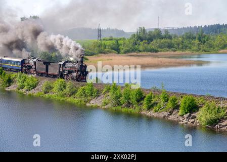 KARELIEN, RUSSLAND - 11. JUNI 2022: Eine alte zweiteilige Dampflokomotive mit Touristenzug fährt in den Damm ein. Karelien, Russland Stockfoto