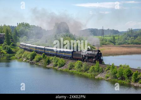 KARELIEN, RUSSLAND - 11. JUNI 2022: Eine alte Dampflokomotive mit einem Touristenzug „Ruskealsky Express“ auf einem Eisenbahndamm. Karelien, Russland Stockfoto