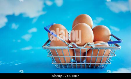 Frische, rohe Hühnereier in einem Mini-Supermarkt-Einkaufskorb, Online-Shopping-Konzept für Lebensmittel oder Lebensmittelgeschäfte und Warenauswahl, Pastellblau Stockfoto