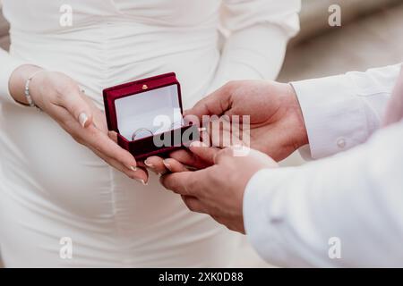 Eine Braut und ein Bräutigam tauschen während ihrer Zeremonie Eheringe aus, wobei die Braut die Ringbox hält und der Bräutigam ausstreckt, um sie zu empfangen. Stockfoto