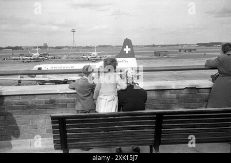 Heathrow, London. 1957: Zwei kleine Kinder und ihre Mutter beobachten Flugzeuge von der Aussichtsplattform am Flughafen London. Direkt vor ihnen befindet sich ein Convair CV-440 Metropolitan Airliner, das von Swissair betrieben wird. In der Ferne befinden sich zwei British European Airways Vickers Viscount Flugzeuge. Stockfoto