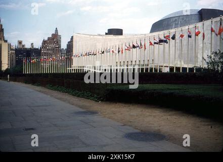 New York, USA. September 1959: Blick auf das Hauptquartier der Vereinten Nationen (UN) im Stadtteil Turtle Bay in Midtown Manhattan in New York City. Der Komplex wurde 1952 fertiggestellt und von einem Architekturausschuss unter der Leitung von Wallace Harrison entworfen und vom Architekturbüro Harrison & Abramovitz errichtet. Vor dem Gebäude befindet sich eine Reihe von Flaggen, die die Mitgliedstaaten der Vereinten Nationen repräsentieren. Stockfoto