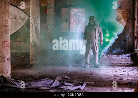 Eine Person in einem chemikalienbeständigen Anzug OP1 vor einem Hintergrund von Ruinen und Rauch einer grünen Rauchkerze. Stockfoto