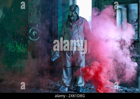 Otwock, Polen - Oktober 2022: Eine Person in einem chemikalienbeständigen militärischen Anzug OP1 vor einem Hintergrund von Ruinen und Rauch einer roten Rauchkerze. Stockfoto