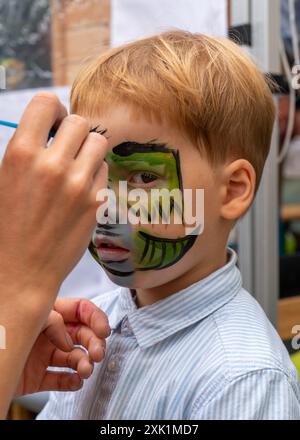 Das Gesicht eines kleinen Jungen mit einem Muster im Gesicht. Der Künstler zeichnet ein Bild von einem grünen Drachen auf das Gesicht eines Kindes Stockfoto